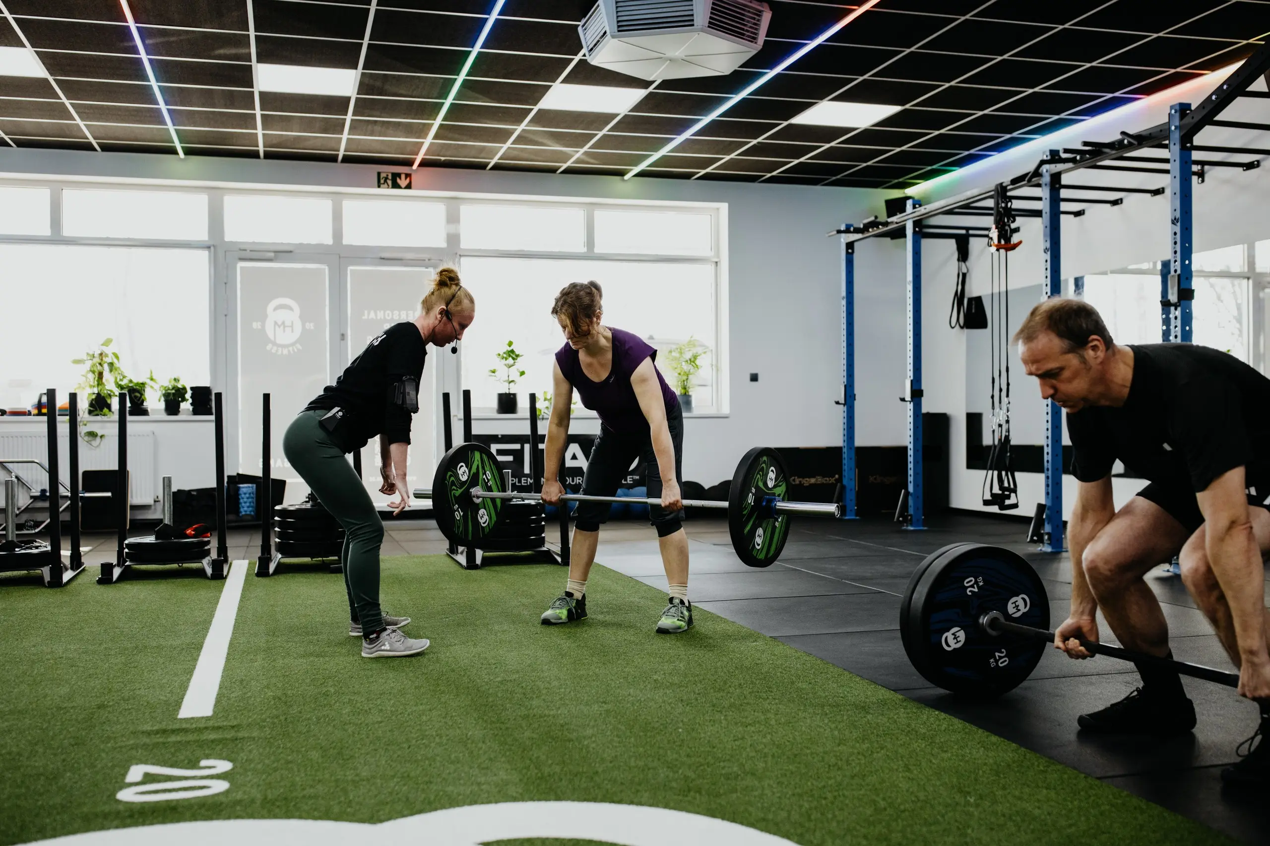 Coach begleitet drei Mitglieder beim Kreuzheben im Semi Private Training