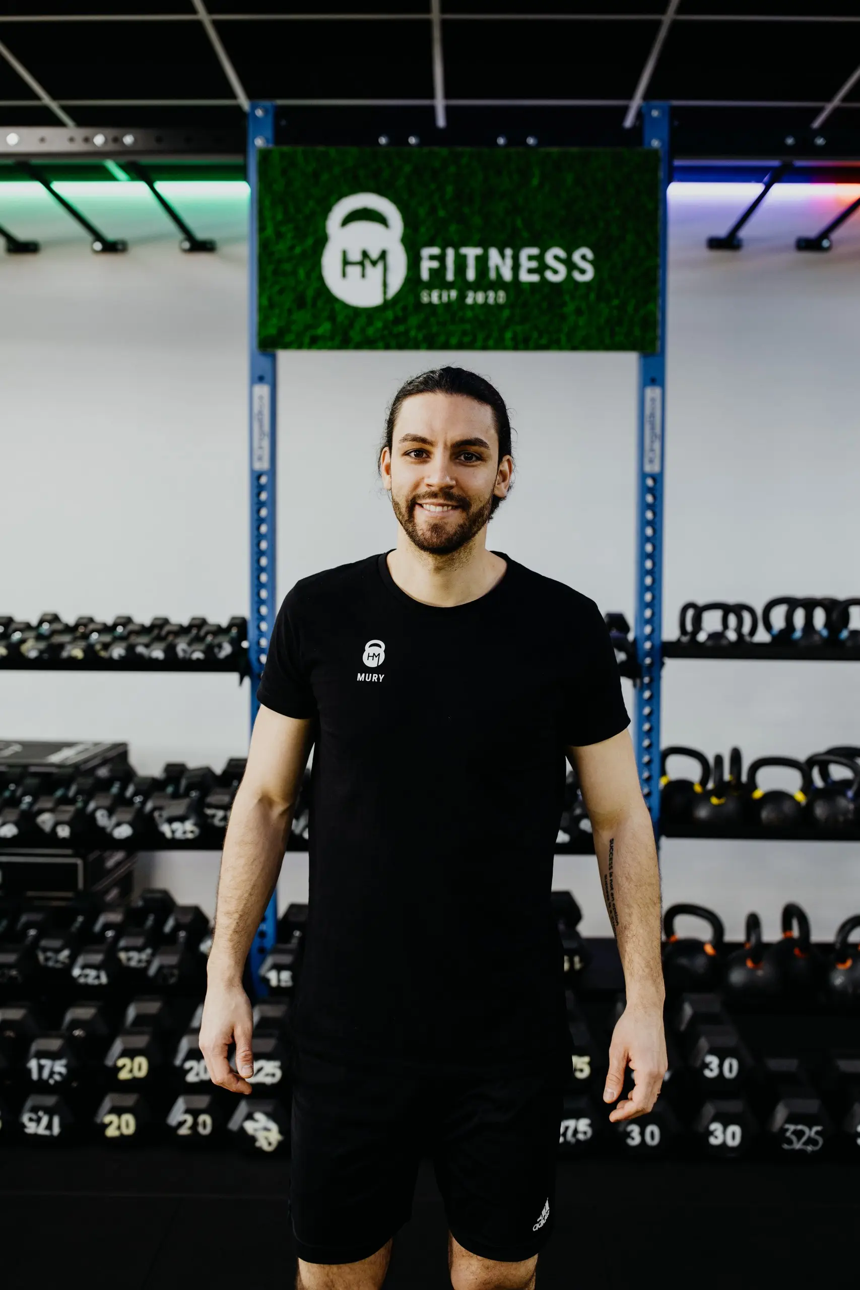 Coach Mury vor dem HM Fitness Schild im Studio